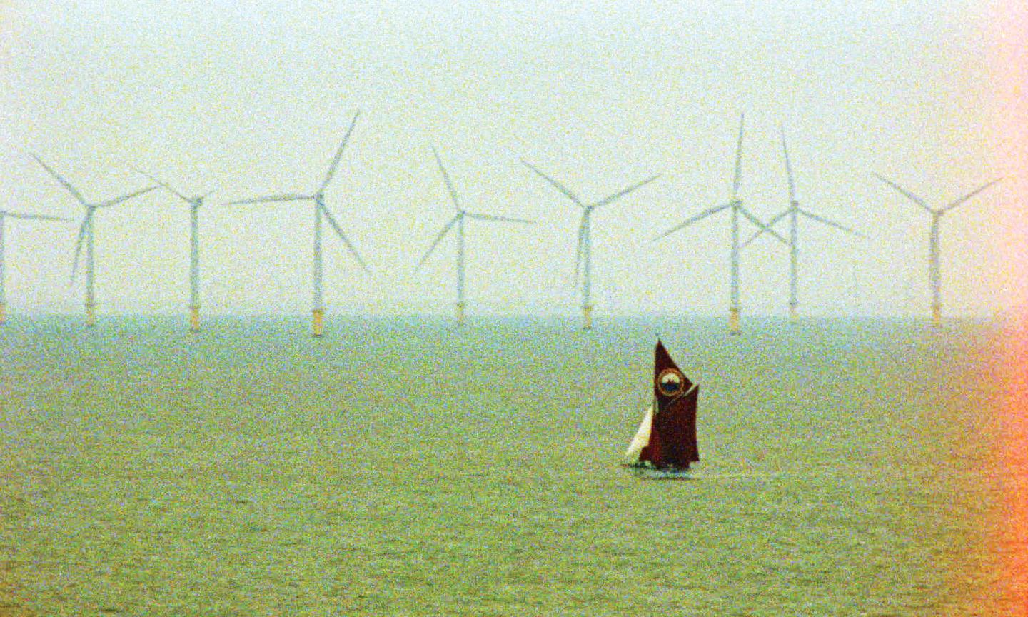 sailing vessel with sails up seen in foreground, with a sea of wind turbines behind.