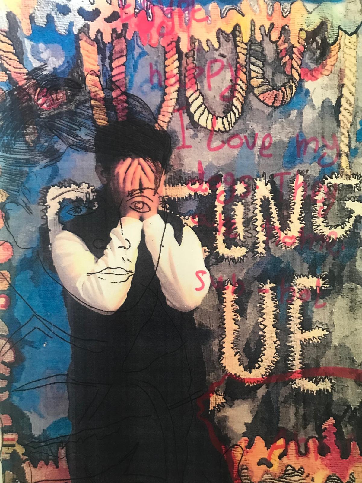 A person stands in front of a colourful artwork, their hands covering their face