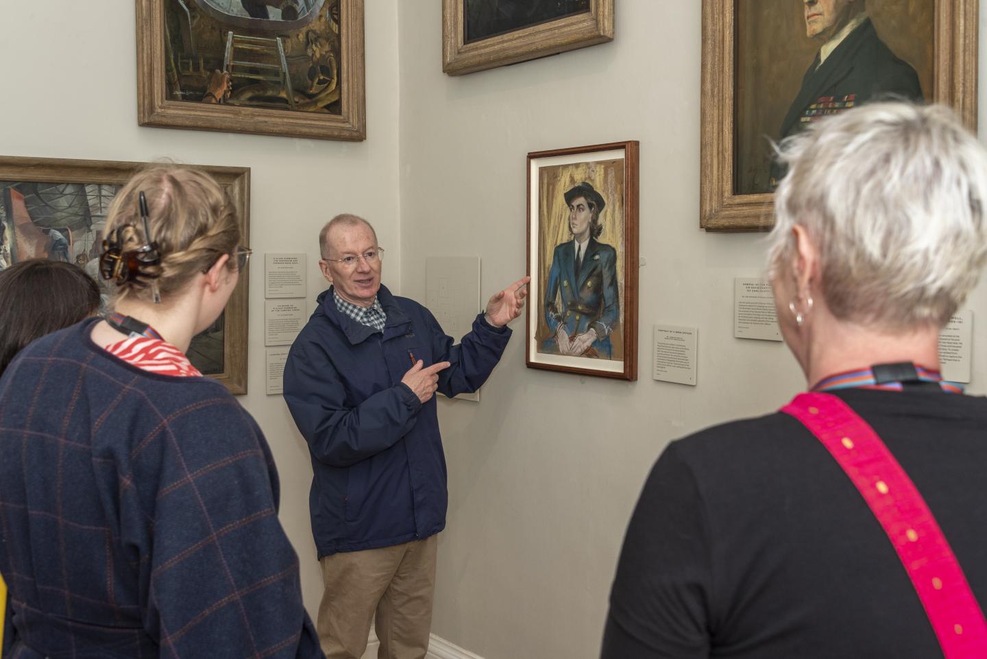 A group of visitors listen to a guide discussing a painting
