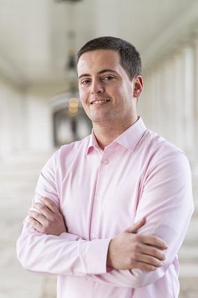 Image of Matthew with arms folded wearing a pink shirt under the Queen's House colonnades