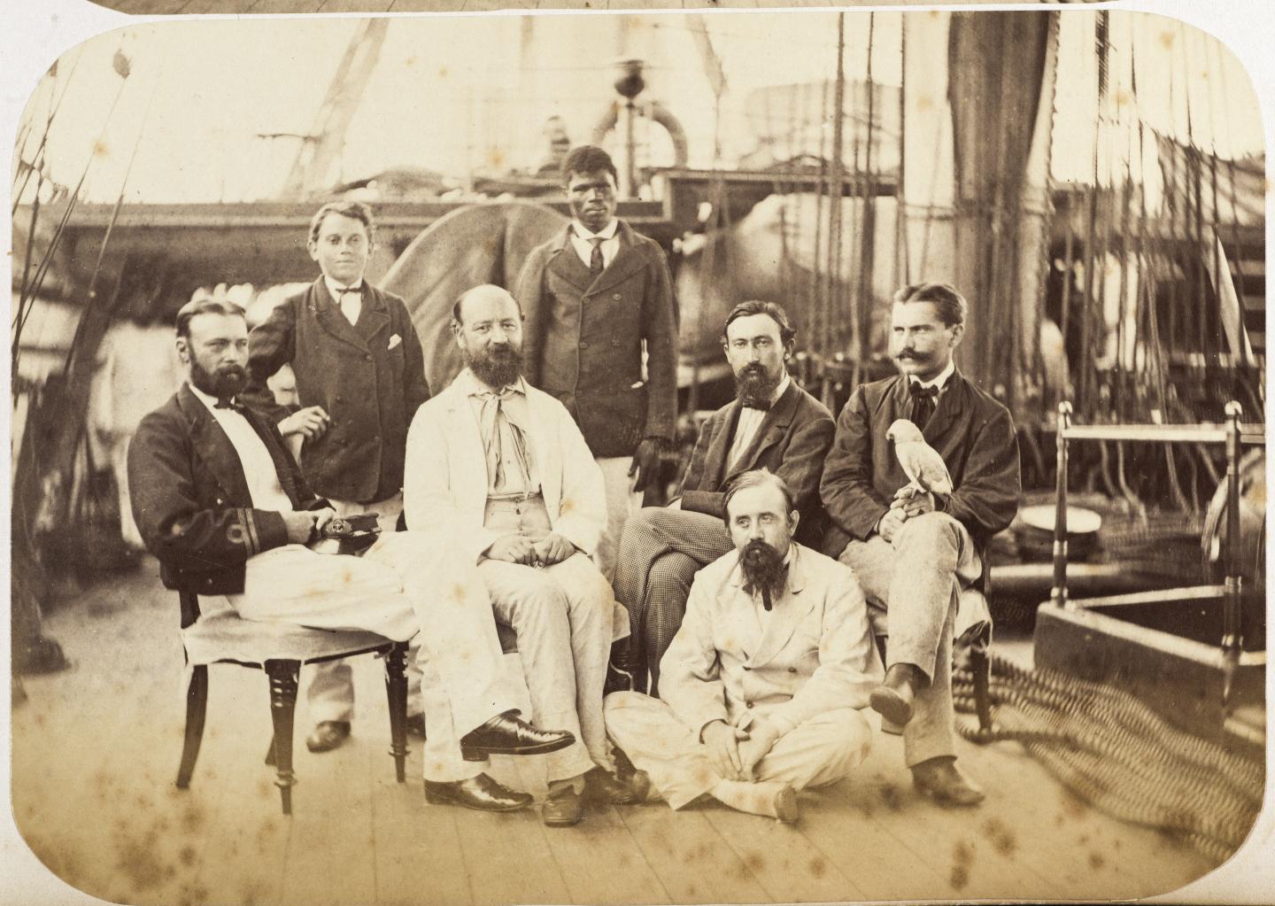 Sepia-tone photograph taken on board HMS Challenger showing the naturalists and two of their assistants, part of an album of photographs from the Challenger expedition of 1875