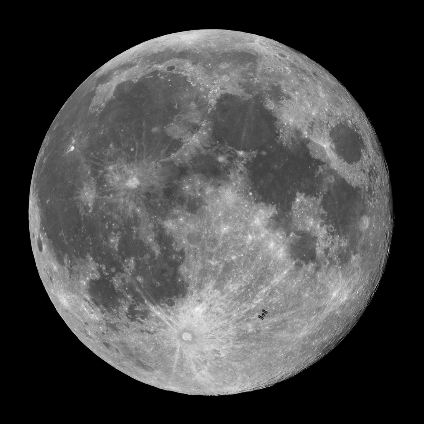 Square image of a full moon in bright white, silver and grey against a black sky. Many impact craters stand out in bright white highlight. In the bottom right hand of the Moon, the International Space Station is visible silhouetted