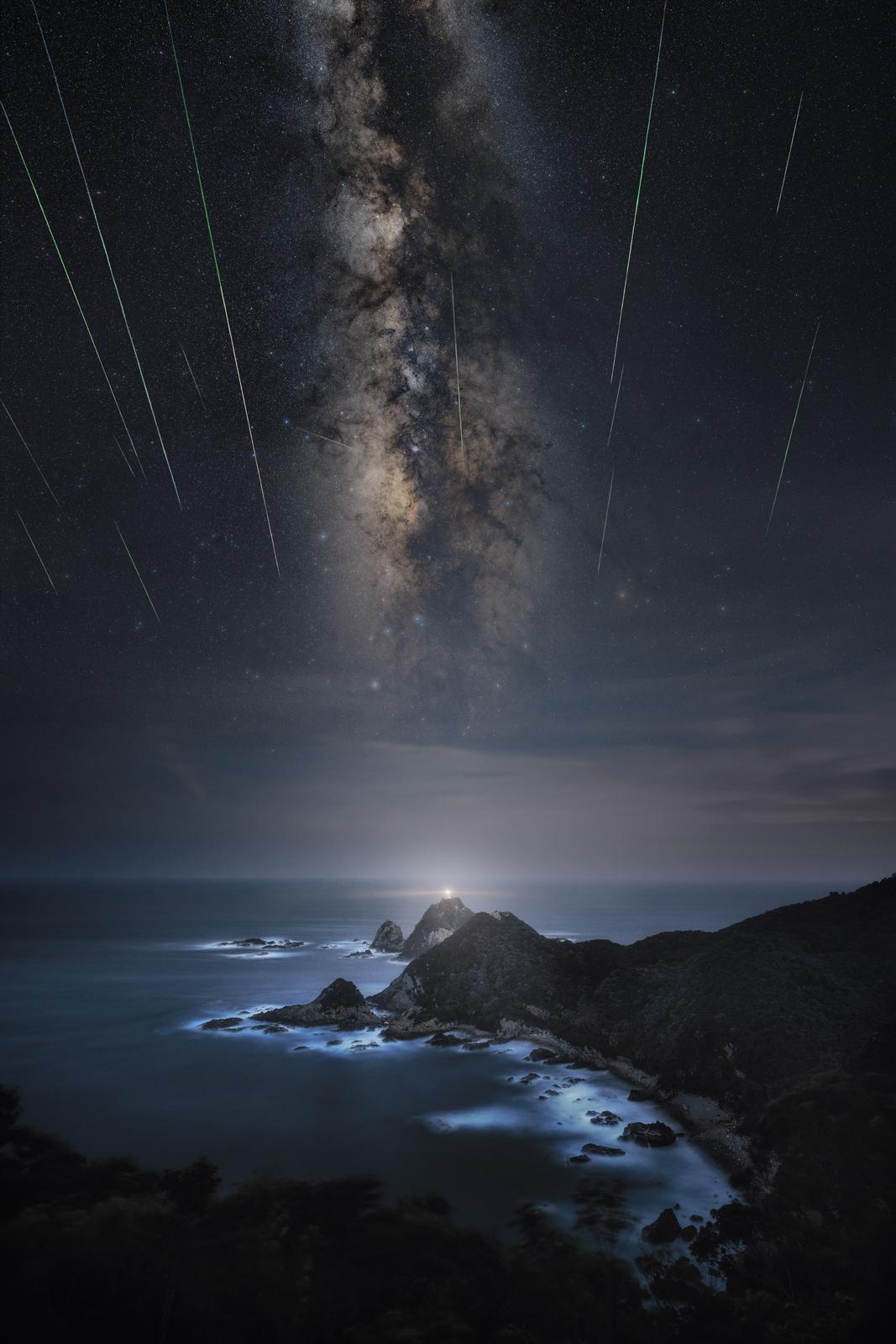 Meteor shower stretching over a lighthouse on a rocky promontory