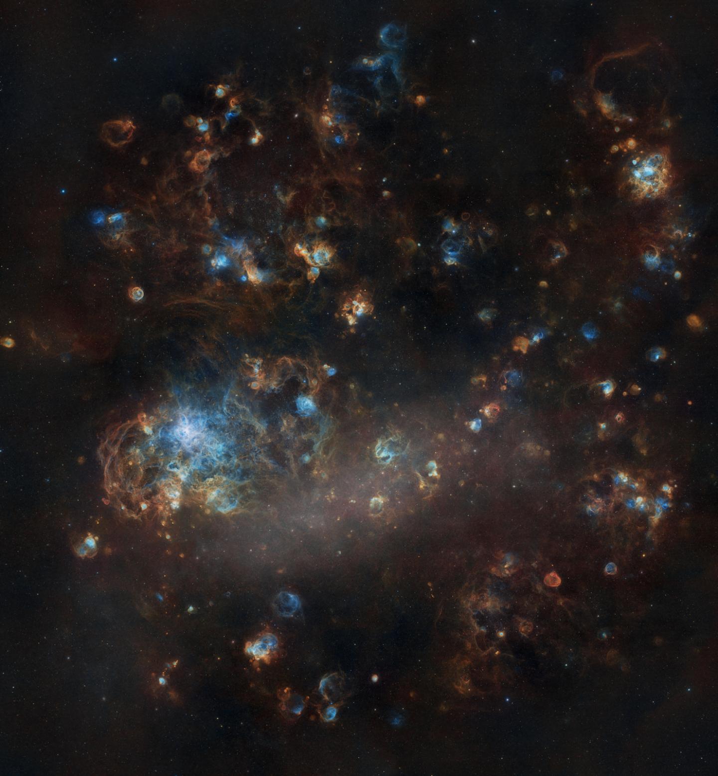 Square image showing an irregular Galaxy, which resembles clouds of gas and dust in dark browns, with lighter brown clouds around the image and in points there are small bright blue circles dotted around the rest of the cloud. In the left middle of the image there is a bigger bright blue patch of gases. 