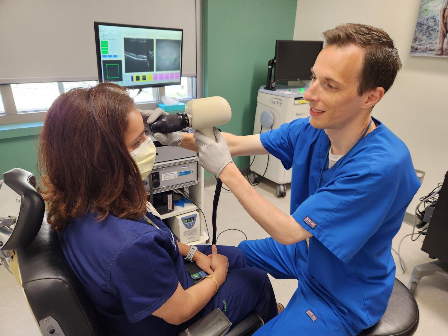 Image of an Ophthalmic Photographer wearing blue scrubs at Work photographing a woman's eye