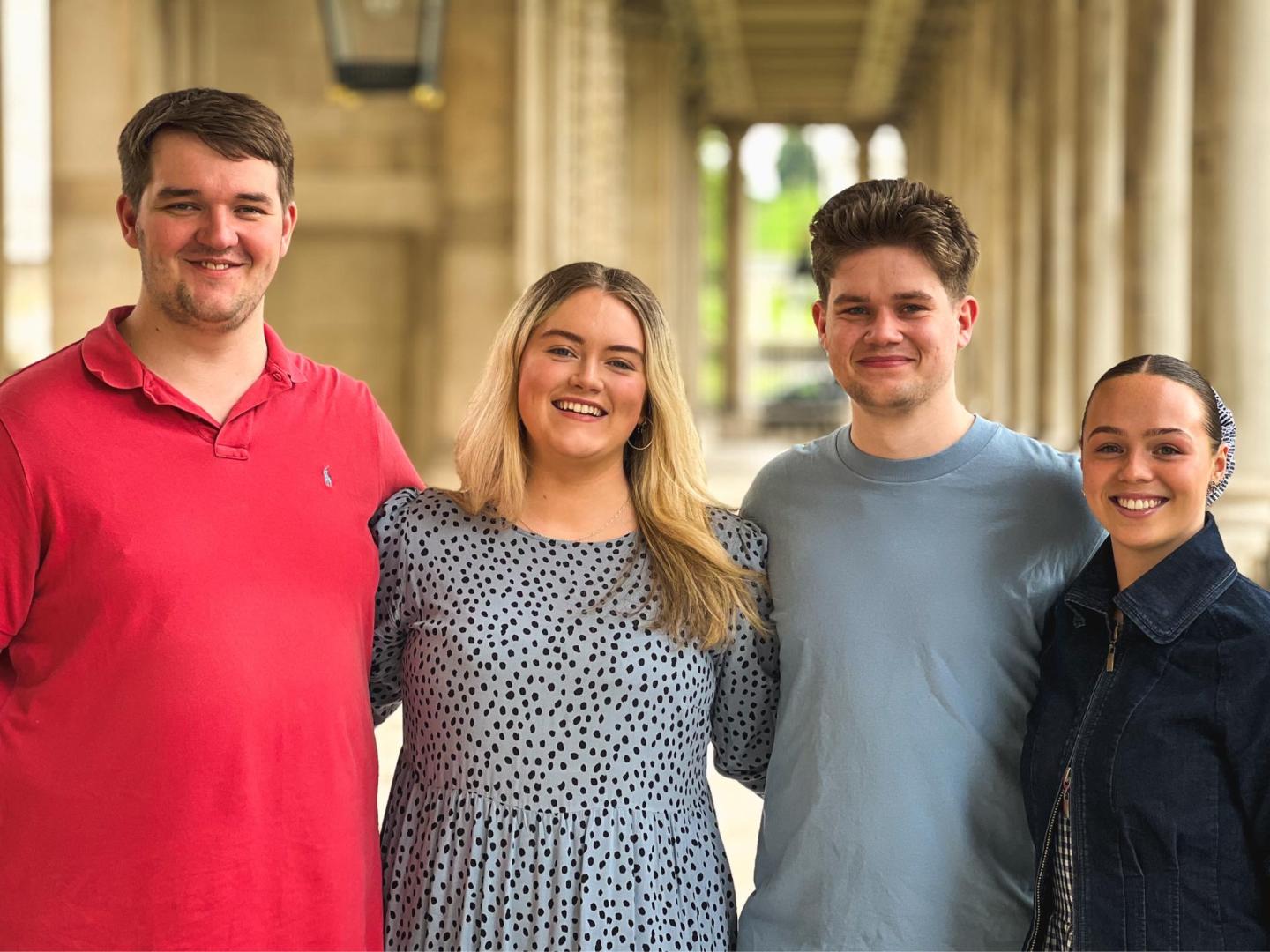 A group of four people with their arms around each other outside the Old Royal Naval College 