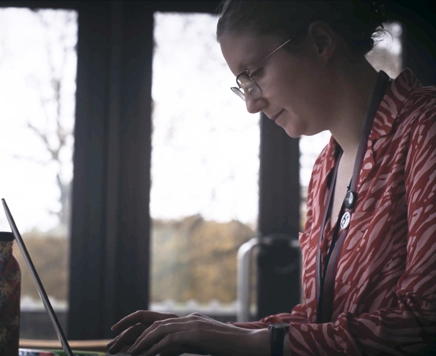 Curator Katherine Gazzard works on a laptop by a window with views of Greenwich Park