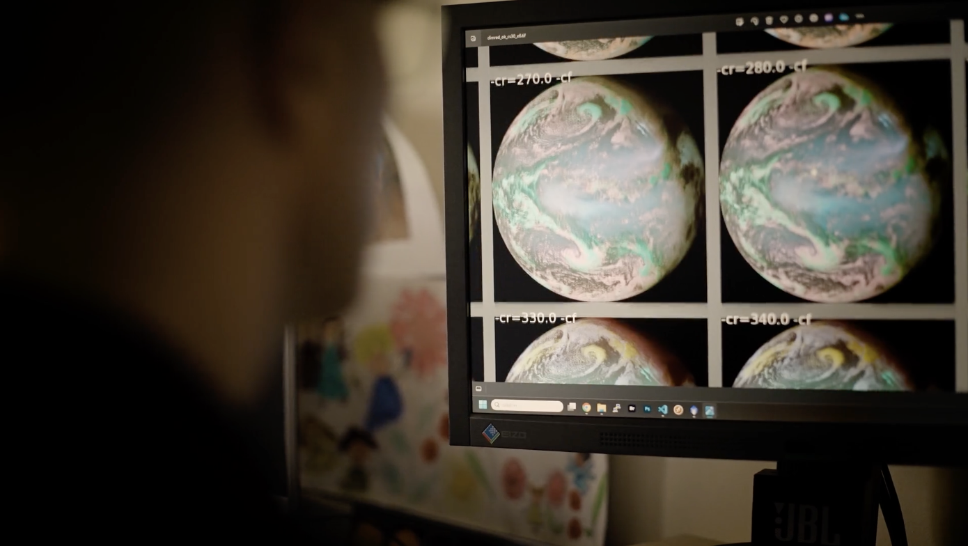 Photo showing the back of Sergio's head as he looks at a computer screen on which there are multiple squares of Earth rendered in different colours including blues and greens