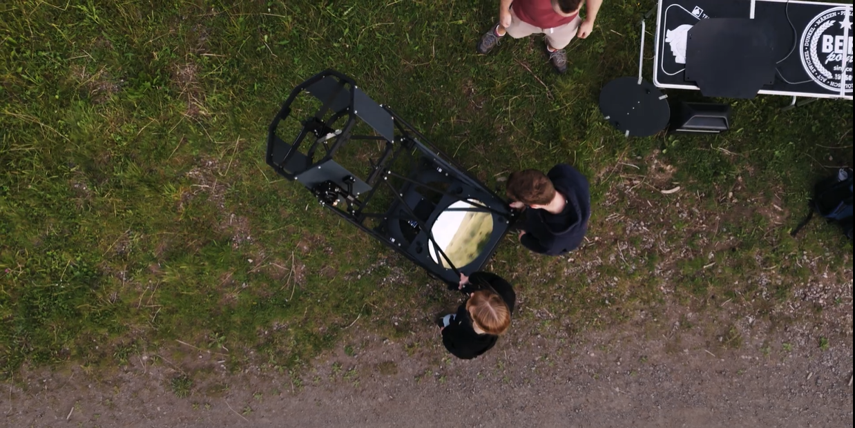 Photo from above looking down at two people adjusting a large telescope which has a large metal frame