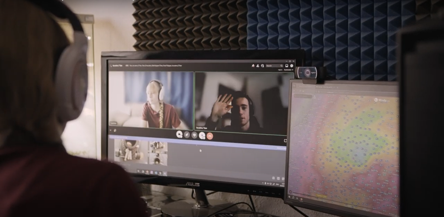 Photo with the back of a woman's head in the left hand corner looking at her computer screen, which shows that she is on a video call with a young man