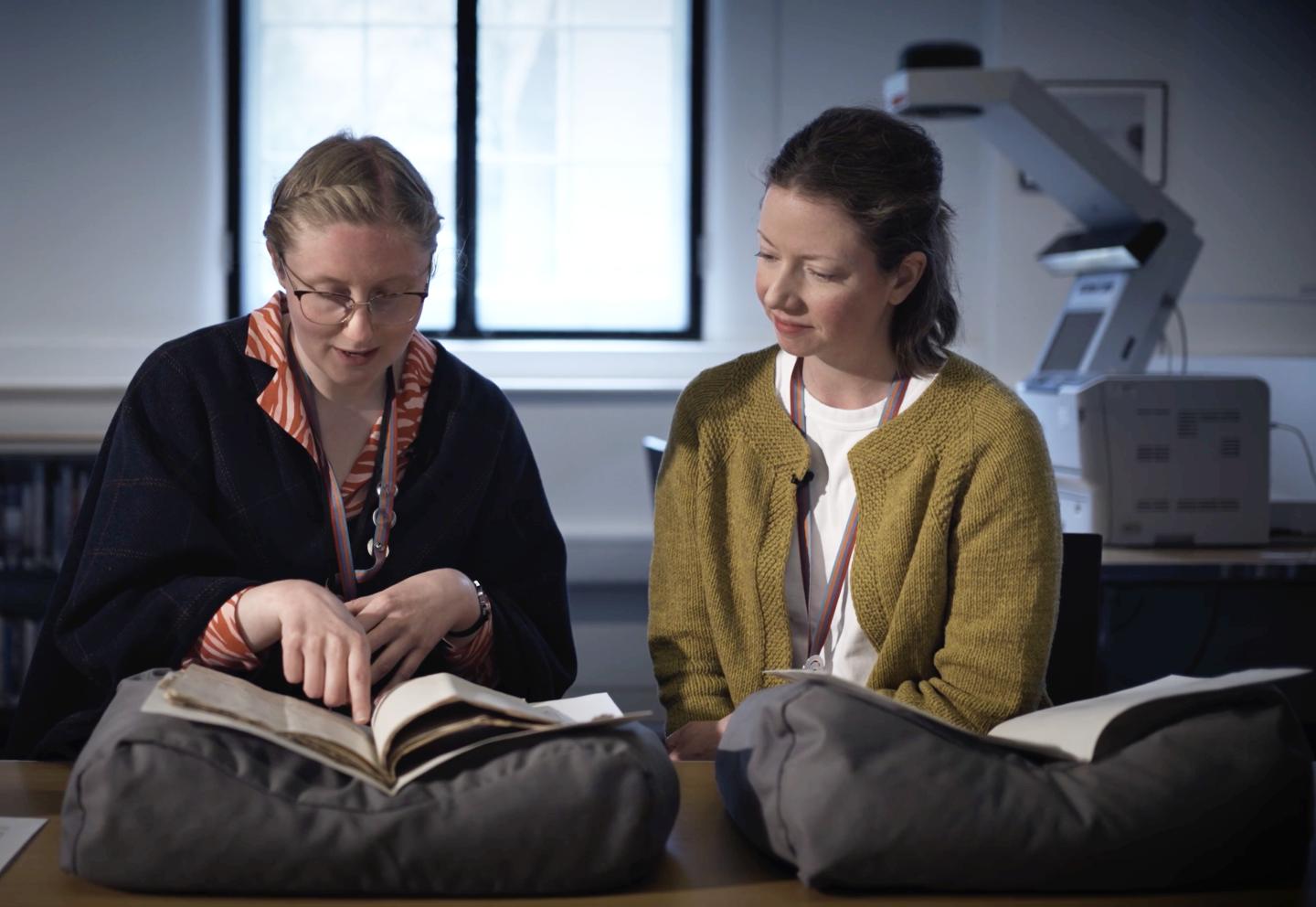 Two people look at a manuscript in a library