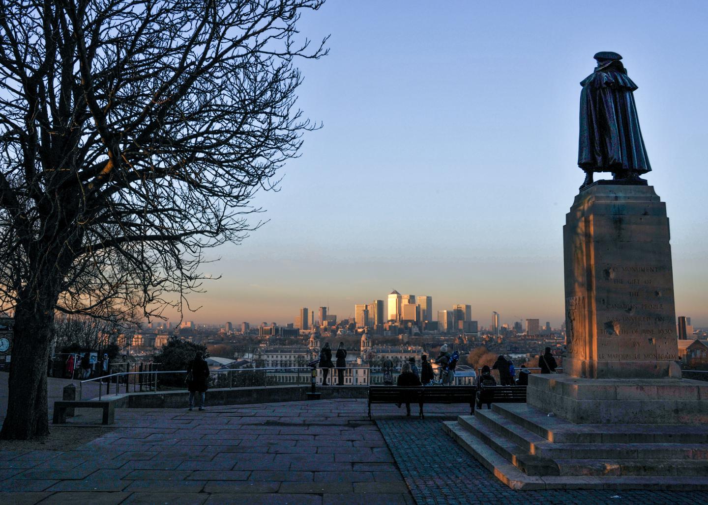 View from the Wolfe Statue at the top of Greenwich Park at dusk, with the skyscrapers of Canary Wharf visible in the distance