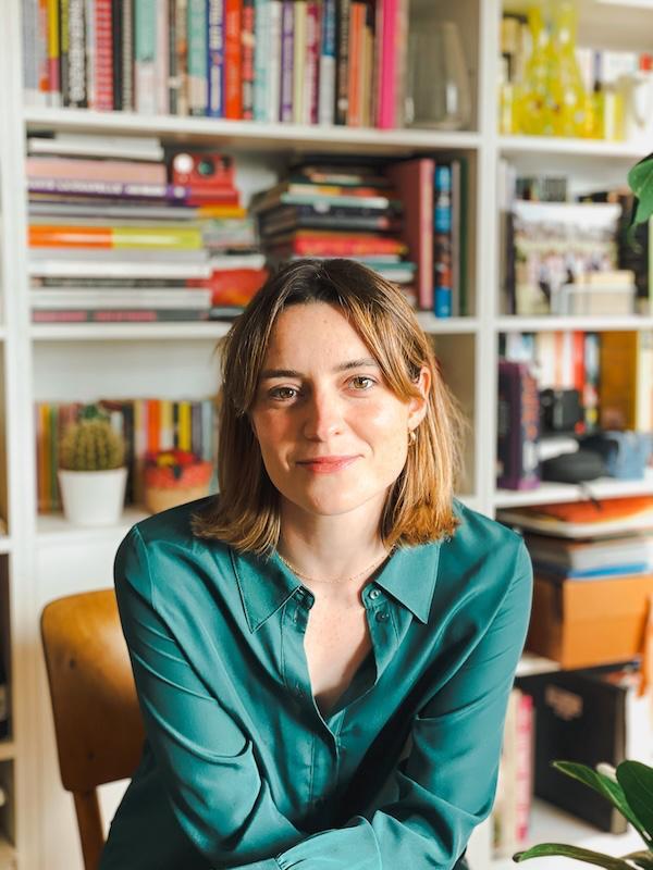 Frankie Evans sat on a chair, wearing a green shirt, brown shoulder length hair 