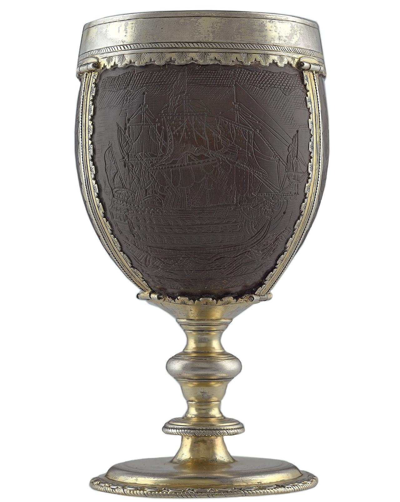 A drinking cup. The cup itself is made out of a carved coconut shell, set within a silver frame and handle