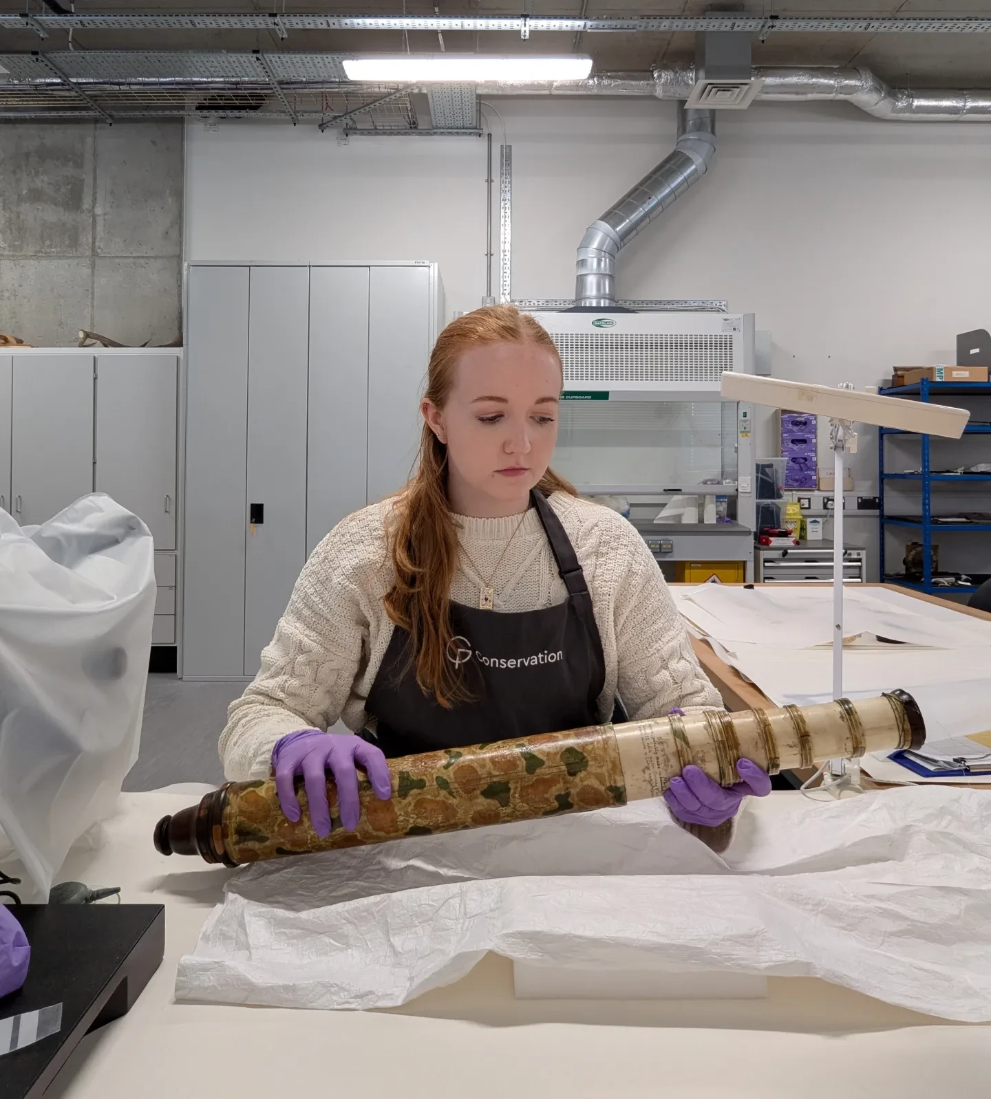 A museum conservator wearing purple gloves handles a 17th century telescope