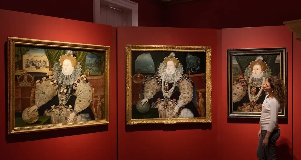 A visitor walks past three similar paintings of Elizabeth the first.